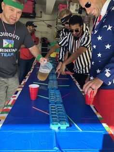 three men standing around a table with cups on it and one man holding a plastic cup