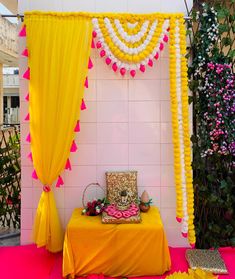 a decorated stage with yellow drapes and pink flowers on the floor, along with other decorations