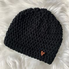 a black crocheted beanie with a heart on the side sitting on white fur