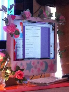 a computer monitor sitting on top of a desk next to a vase filled with flowers