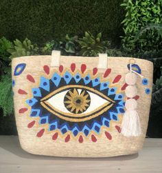 This evil eye beach bag is a woven beach tote, perfect as a summer bag and a thoughtful gift for her. This boho market tote bag showcases a Mediterranean style, ideal for vacation shopping. The tassel bag offers evil eye protection and serves as a stylish beach tote for summer. Stylish and Protective: The Evil Eye Woven Tote Bag Handwoven tote bag featuring a painted evil eye design for protection and style Perfect for the beach, market, shopping, vacation, or everyday use Bohemian-inspired desi Sand-colored Woven Tote Beach Bag, Sand-colored Straw Bag For Beach Season, Sand Straw Bag For Beach Season, Sand Colored Tote Beach Bag, Sand-colored Tote Beach Bag, Sand-colored Tote Beach Bag For Beach Season, Sand Colored Jute Bag For Beach Season, Eco-friendly Sand Colored Tote Beach Bag, Eco-friendly Sand-colored Tote Beach Bag