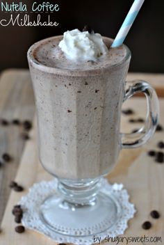 a glass cup filled with coffee and whipped cream on top of a wooden table next to chocolate chips