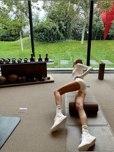 a woman in white shirt and shorts sitting on yoga mat with her legs spread out