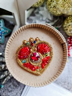 a heart shaped brooch sitting on top of a cardboard box next to christmas ornaments