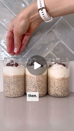 three jars filled with food sitting on top of a counter next to a person's hand