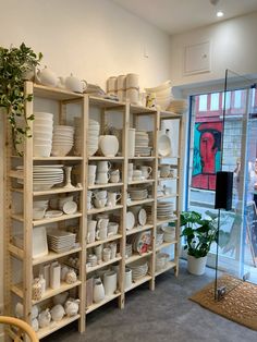 a room filled with lots of white plates and bowls on wooden shelves next to a window