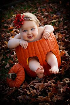 a baby sitting in a pumpkin costume on the ground with leaves around her and looking at the camera