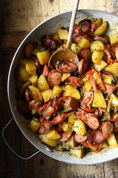 a pan filled with potatoes and sausage on top of a wooden table