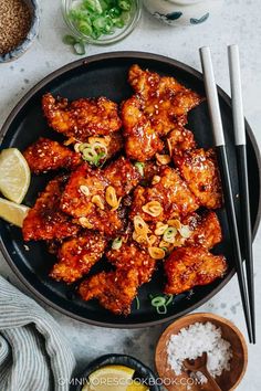 a black plate topped with fried chicken next to rice and chopsticks