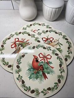 four christmas coasters with holly and cardinals on them, sitting on a counter top