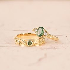 two gold wedding rings with green and white stones