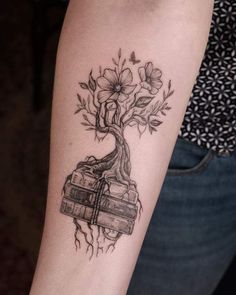 a woman's arm with a tattoo on it and a tree growing out of books