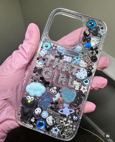 someone wearing pink gloves holding up a phone case that has various buttons and charms on it