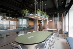 a man standing in an office looking at a table with chairs and plants hanging from the ceiling