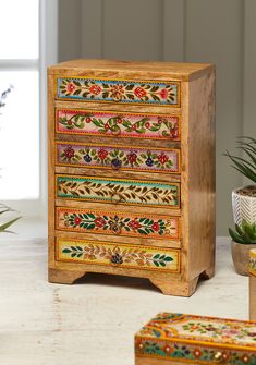 a multicolored wooden chest of drawers next to potted plants on a table