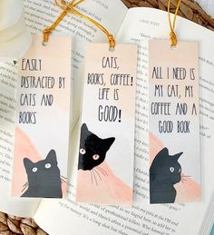 three bookmarks with black cats on them sitting next to each other in front of an open book