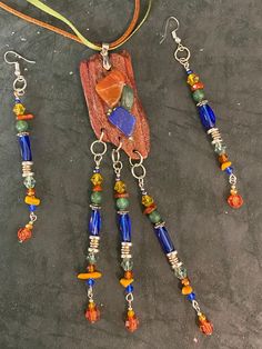 This pendant set has a decidedly Southwestern flair to it. Natural wood with a sheen of barely-there rose gold paint covers the surface of the pendant, followed by a cluster of stones in carnelian, lapis, and green agate. Little tiny light green crystals peek from between the stones. Along the bottom, long, dangling beads in a southwestern pallet finish the piece with a swish! The pendant measures 6 inches in length X 1inch in width X 0.25 inches in height. The earrings are 4 inches long from the top of the wire Light Green Crystals, Rose Gold Paint, Rose Gold Painting, Jewelry Rustic, Southwestern Jewelry, Green Agate, Green Crystals, Beaded Dangles, Gold Paint