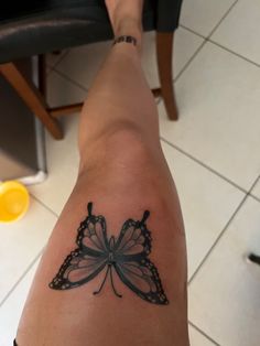 a woman's leg with a butterfly tattoo on the back of her arm, sitting in front of a chair