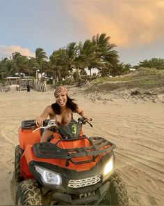 a woman riding an orange four wheeler on top of a sandy beach next to palm trees