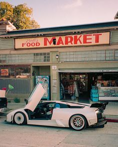 a white sports car parked in front of a food market with its door open and the hood up