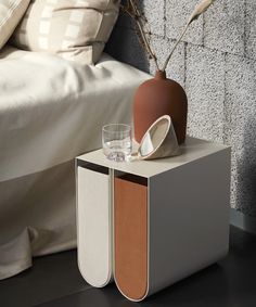 an orange vase sitting on top of a white table next to a bed with pillows