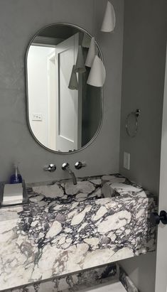 a bathroom sink with marble counter top next to a mirror and light fixture above it