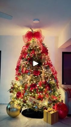 a christmas tree decorated with red and gold ornaments in a living room next to a tv