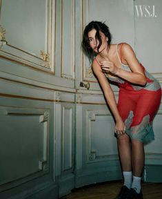 a woman in red and grey dress leaning against wall