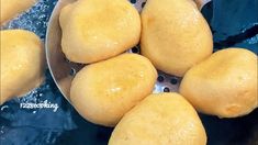 several round yellow bread rolls in a metal strainer on a blue counter top with water droplets around them