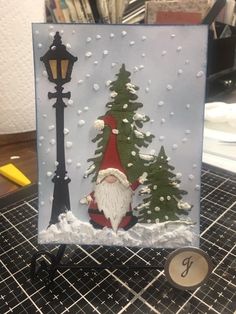 a christmas card with a santa clause standing next to a lamp post and snow covered trees