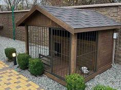 a small wooden dog house in the middle of some gravel and rocks with bushes around it