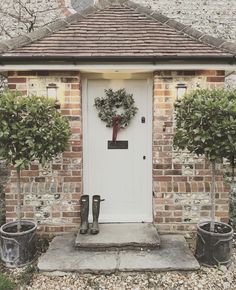 a brick house with wreaths on the front door and two potted plants outside