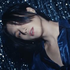 a woman with dark hair and blue dress posing in front of sequins background