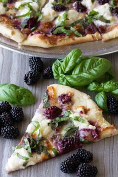 two slices of pizza with blackberries and spinach leaves on the side next to each other