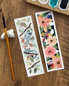 two bookmarks with flowers and leaves on them next to paintbrushes, watercolors and paper