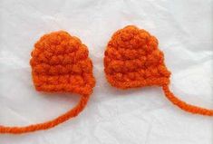 two orange crocheted hats sitting on top of a white tablecloth covered floor