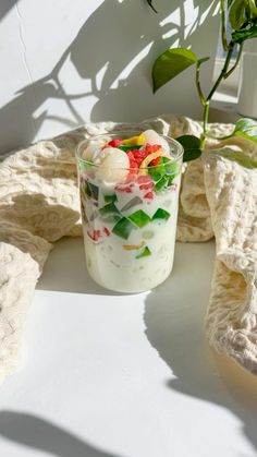 a glass filled with food sitting on top of a table next to a potted plant