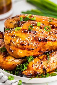 grilled chicken with sesame seeds and green onions on a white plate next to asparagus