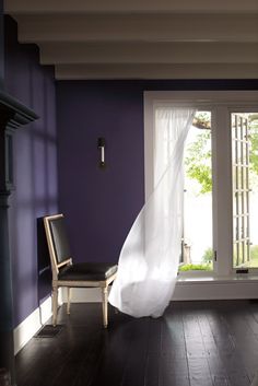 an empty room with purple walls and white drapes hanging from the ceiling, next to a chair