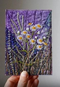 a hand holding up a piece of paper with daisies in the center and purple background