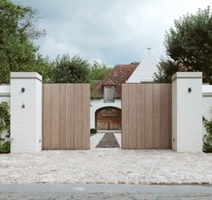 an entrance to a house that is made out of white bricks and wooden doors, with a brick pathway leading into it