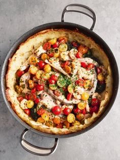 a pan filled with chicken and tomatoes on top of a table