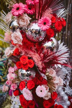 a red and white christmas tree decorated with silver balls, pink flowers and feathers on it