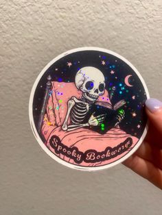 a person holding up a sticker with a skeleton reading a book in bed at night