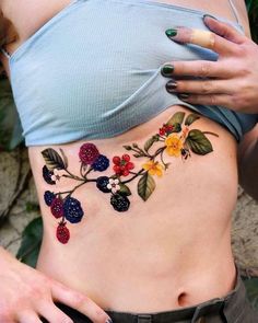 a woman's stomach with berries and leaves tattoo on her side, which is decorated with multicolored flowers