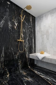 a bathroom with black marble walls and flooring, shower head and hand held faucet