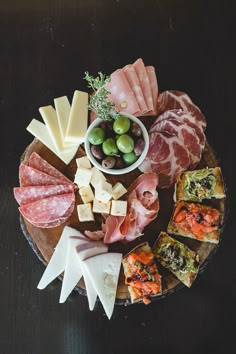 an assortment of cheeses, meats and olives on a wooden platter