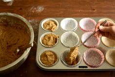 someone using a spatula to mix batter into cupcakes in muffin tins