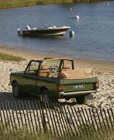 an old pick up truck parked on the beach with boats in the water behind it