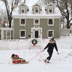 a woman pulling a child in a sleigh through the snow near a house